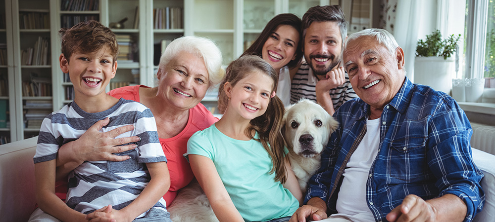 Auf dem Bild ist eine Familie mit Kindern zu sehen, die Besuch von den Großeltern und ihrem Hund hat.